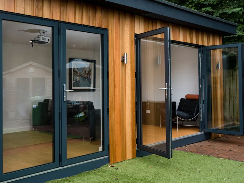 Anthracite grey aluminium bifold doors open on a garden room with timber cladding